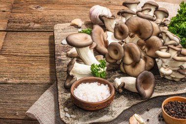 Oyster mushrooms ready for cooking. Fresh parsley, spices and garlic. Trendy hard light, dark shadows, old wooden background, copy space
