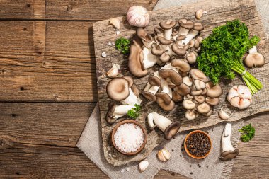 Oyster mushrooms ready for cooking. Fresh parsley, spices and garlic. Trendy hard light, dark shadows, old wooden background, top view
