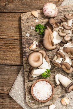 Oyster mushrooms ready for cooking. Fresh parsley, spices and garlic. Trendy hard light, dark shadows, old wooden background, top view