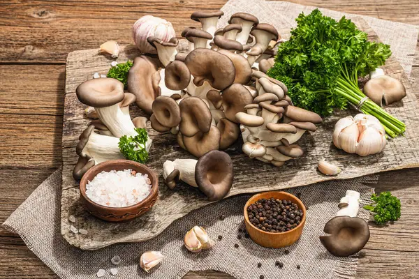 Oyster mushrooms ready for cooking. Fresh parsley, spices and garlic. Trendy hard light, dark shadows, old wooden background, close up