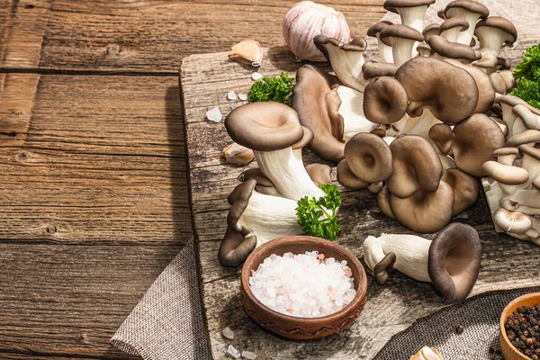 Oyster mushrooms ready for cooking. Fresh parsley, spices and garlic. Trendy hard light, dark shadows, old wooden background, copy space
