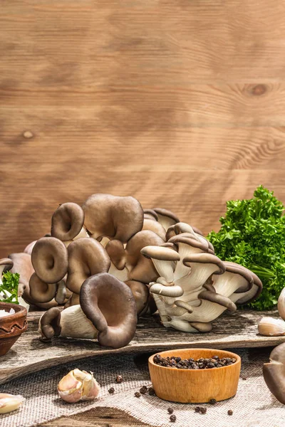 Oyster mushrooms ready for cooking. Fresh parsley, spices and garlic. Trendy hard light, dark shadows, old wooden background, copy space