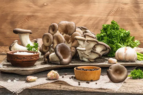 Oyster mushrooms ready for cooking. Fresh parsley, spices and garlic. Trendy hard light, dark shadows, old wooden background, copy space