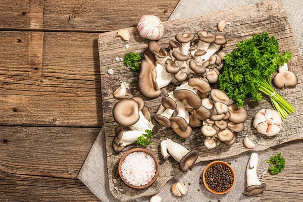 Oyster mushrooms ready for cooking. Fresh parsley, spices and garlic. Trendy hard light, dark shadows, old wooden background, top view