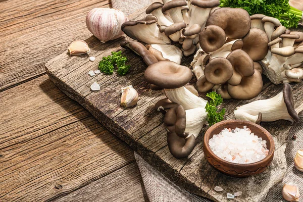 Oyster mushrooms ready for cooking. Fresh parsley, spices and garlic. Trendy hard light, dark shadows, old wooden background, copy space