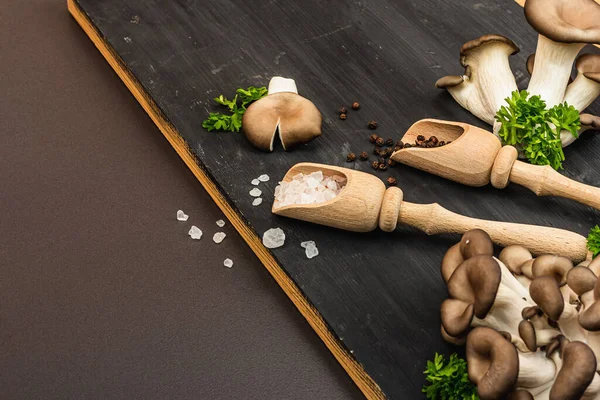 Delicious organic oyster mushrooms with spices and fresh parsley on wooden cutting board. Source of beta glucan, black stone concrete background, copy space