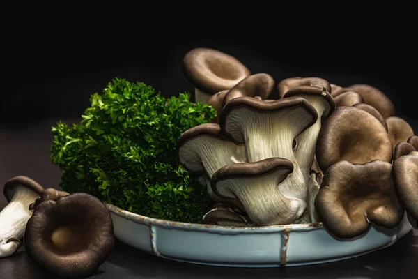 Delicious organic oyster mushrooms with fresh parsley. Source of beta glucan, black stone concrete background, close up
