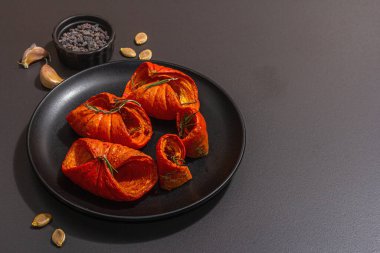 Baked pumpkin slices with honey, spices and seeds. Healthy vegan food, trendy hard light, dark shadow. Black stone concrete background, flat lay, copy space