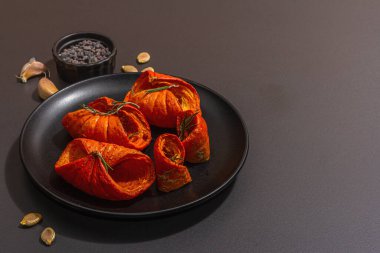 Baked pumpkin slices with honey, spices and seeds. Healthy vegan food, trendy hard light, dark shadow. Black stone concrete background, flat lay, copy space
