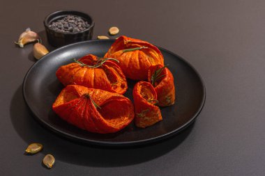 Baked pumpkin slices with honey, spices and seeds. Healthy vegan food, trendy hard light, dark shadow. Black stone concrete background, flat lay, copy space