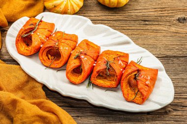 Baked Hokkaido pumpkin with sauce, spices and honey. Healthy vegan food, dry rosemary, modern hard light, dark shadow. Black stone concrete background, close up