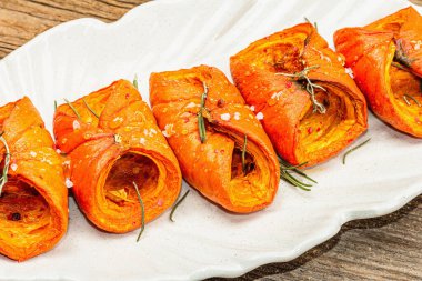 Baked Hokkaido pumpkin with sauce, spices and honey. Healthy vegan food, dry rosemary, modern hard light, dark shadow. Black stone concrete background, close up