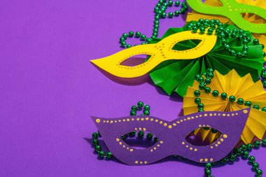 Festive Mardi Gras masquerade purple background. Fat Tuesday carnival, masks, beads, traditional decor. Symbolic colors, trendy hard light, dark shadow, flat lay, copy space