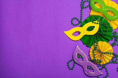 Festive Mardi Gras masquerade purple background. Fat Tuesday carnival, masks, beads, traditional decor. Symbolic colors, trendy hard light, dark shadow, flat lay, top view