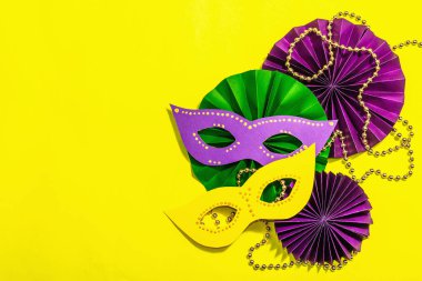 Festive Mardi Gras masquerade yellow background. Fat Tuesday carnival, masks, beads, traditional decor. Symbolic colors, trendy hard light, dark shadow, flat lay, top view