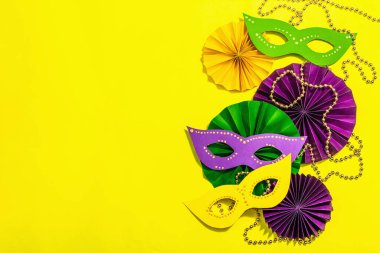 Festive Mardi Gras masquerade yellow background. Fat Tuesday carnival, masks, beads, traditional decor. Symbolic colors, trendy hard light, dark shadow, flat lay, top view