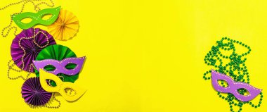 Festive Mardi Gras masquerade yellow background. Fat Tuesday carnival, masks, beads, traditional decor. Symbolic colors, trendy hard light, dark shadow, flat lay, banner format