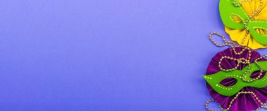 Festive Mardi Gras masquerade violet background. Fat Tuesday carnival, masks, beads, traditional decor. Symbolic colors, trendy hard light, dark shadow, flat lay, banner format