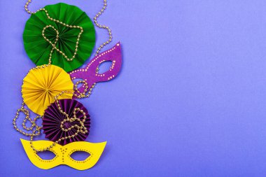 Festive Mardi Gras masquerade violet background. Fat Tuesday carnival, masks, beads, traditional decor. Symbolic colors, trendy hard light, dark shadow, flat lay, top view