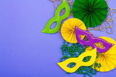 Festive Mardi Gras masquerade violet background. Fat Tuesday carnival, masks, beads, traditional decor. Symbolic colors, trendy hard light, dark shadow, flat lay, top view