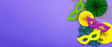 Festive Mardi Gras masquerade violet background. Fat Tuesday carnival, masks, beads, traditional decor. Symbolic colors, trendy hard light, dark shadow, flat lay, banner format