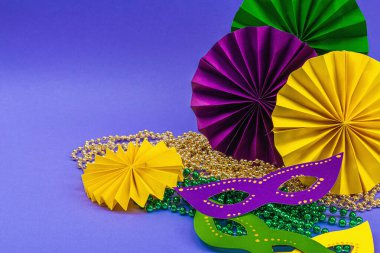 Festive Mardi Gras masquerade violet background. Fat Tuesday carnival, masks, beads, traditional decor. Symbolic colors, trendy hard light, dark shadow, flat lay, copy space