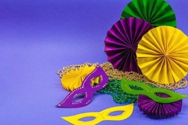 Festive Mardi Gras masquerade violet background. Fat Tuesday carnival, masks, beads, traditional decor. Symbolic colors, trendy hard light, dark shadow, flat lay, copy space