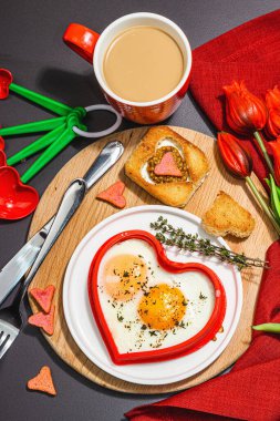 Heart-shaped fried egg served with toasted bread and spices on a plate. Romantic art food idea for Valentine's breakfast. Hard light, dark shadow, black stone concrete background, top view