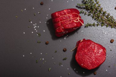 Raw Eye of round steak with spices and herbs on black stone concrete background. A trendy hard light, dark shadow, flat lay, top view