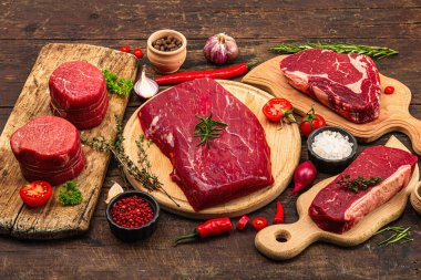 Set of various steaks with traditional spices and herbs. Fresh raw meat cuts includes ribeye, eye round, flank and striploin steaks. Old wooden background, flat lay, copy space