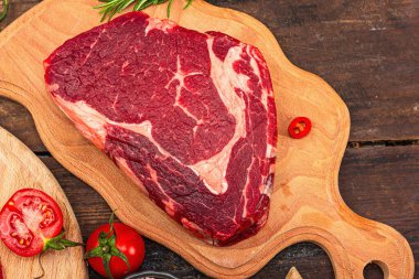 Close up of ribeye steak with traditional spices and herbs. Fresh raw meat cut, old wooden background, flat lay, top view