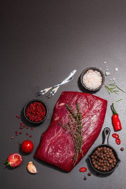 Flank steak with classic spices and herbs. Fresh raw meat cut, modern hard light, dark shadow, black stone concrete background, flat lay, top view