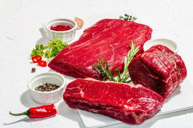 Set of various steaks with spices and herbs. Classic raw meat cuts includes eye round, flank and striploin steaks. Plaster white background, flat lay, close up