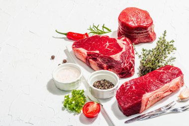 Set of various steaks with spices and herbs. Classic raw meat cuts includes ribeye, eye round and striploin steaks. Plaster white background, flat lay, copy space