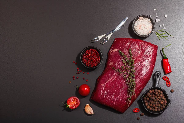 Flank steak with classic spices and herbs. Fresh raw meat cut, modern hard light, dark shadow, black stone concrete background, flat lay, top view