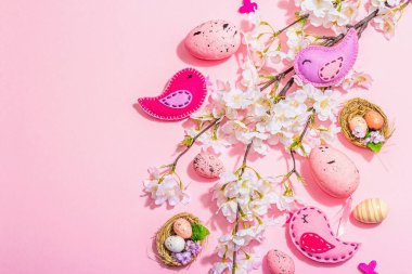 Gentle Easter composition with cherry flowers and handmade felt birds. Decorative eggs and nest, cute rabbits. Hard light, dark shadow, pink background, top view