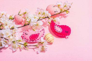 Gentle Easter composition with cherry flowers and handmade felt birds. Decorative eggs and nest, cute rabbits. Hard light, dark shadow, pink background, top view