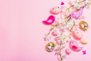 Gentle Easter composition with cherry flowers and handmade felt birds. Decorative eggs and nest, cute rabbits. Hard light, dark shadow, pink background, top view