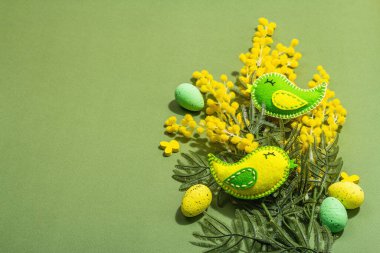 Easter composition with traditional spring flowers and handmade felt birds. Decorative eggs, hard light, dark shadow, savannah green color background, copy space