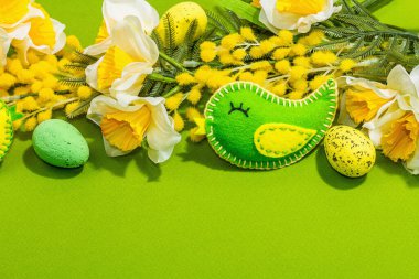 Easter composition with traditional spring flowers and handmade felt birds. Decorative eggs, rabbits, hard light, dark shadow, green background, copy space