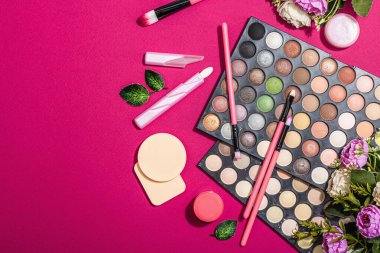Make up set with colorful eyeshadow palettes, brushes, sponges and flowers. Trendy viva magenta color background, spring festive cosmetic concept, flat lay, top view
