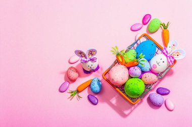Easter sale concept. Shopping basket with festive symbols - rabbit, eggs, bird, and traditional decor. Pastel design, trendy hard light, dark shadow, pink background, top view