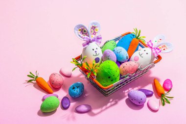 Easter sale concept. Shopping basket with festive symbols - rabbit, eggs, bird, and traditional decor. Pastel design, trendy hard light, dark shadow, pink background, copy space