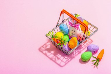 Easter sale concept. Shopping basket with festive symbols - rabbit, eggs, bird, and traditional decor. Pastel design, trendy hard light, dark shadow, pink background, copy space