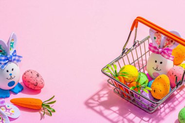 Easter sale concept. Shopping basket with festive symbols - rabbit, eggs, bird, and traditional decor. Pastel design, trendy hard light, dark shadow, pink background, copy space