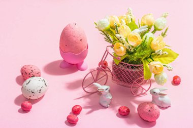 Gentle Easter greeting card with spring flowers, rabbit, eggs and traditional decor. Happy holiday concept, hard light, dark shadow, pink background, close up