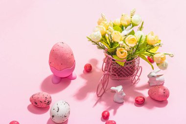 Gentle Easter greeting card with spring flowers, rabbit, eggs and traditional decor. Happy holiday concept, hard light, dark shadow, pink background, close up