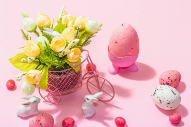 Gentle Easter greeting card with spring flowers, rabbit, eggs and traditional decor. Happy holiday concept, hard light, dark shadow, pink background, close up