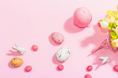Gentle Easter greeting card with spring flowers, rabbit, eggs and traditional decor. Happy holiday concept, hard light, dark shadow, pink background, top view
