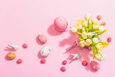 Gentle Easter greeting card with spring flowers, rabbit, eggs and traditional decor. Happy holiday concept, hard light, dark shadow, pink background, top view
